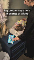 Big brother opens the one-hand pop top and pulls one wipe during a diaper change